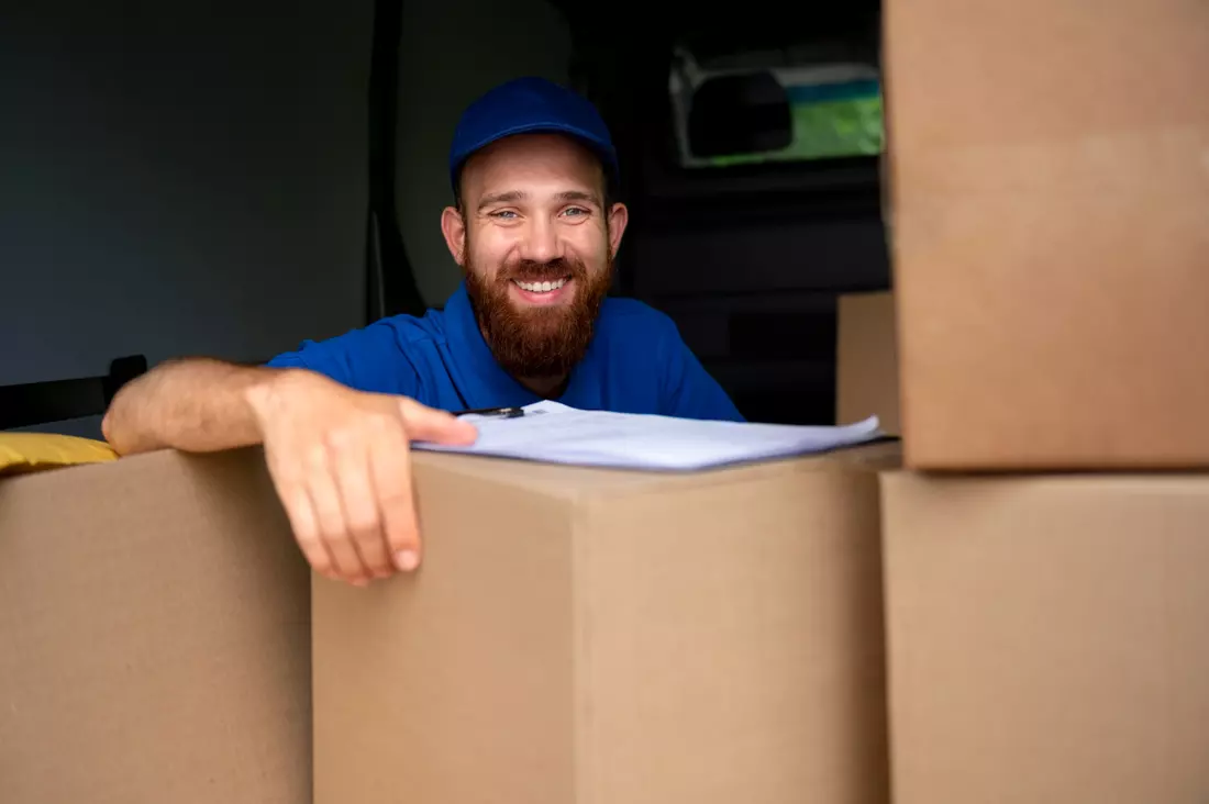 Un déménageur souriant, en tenue de travail, accoudé à des cartons dans son camion